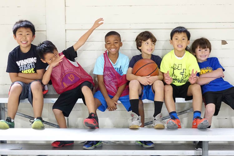 Triple Threat Academy campers seated together with a basketball in an official program photograph